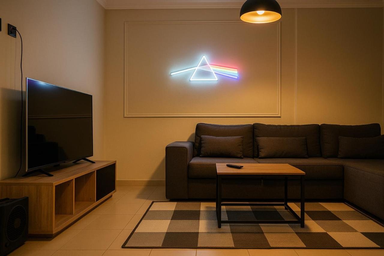 Warmly lit living room at The Prism with the neon prism above a grey sofa and smart TV